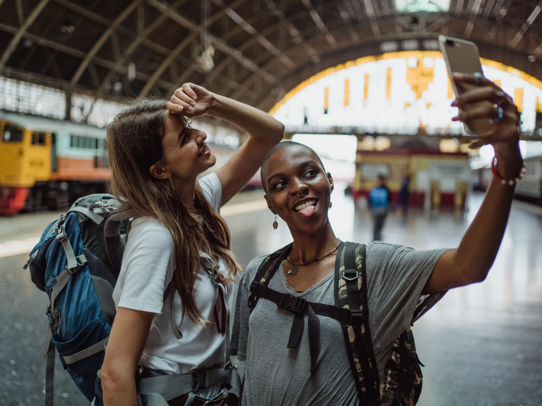 Dos viajeras con mochila se toman una selfie en una estación de tren, conectadas con su eSIM de VuelaSim